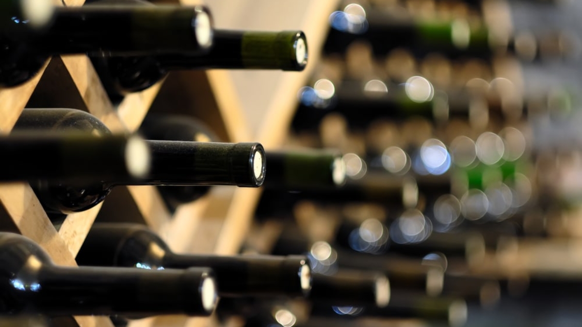 Several wine bottles stored horizontally on wooden racks, with bottle necks facing outward and the background softly blurred, giving a sense of depth and focus on the wine storage.