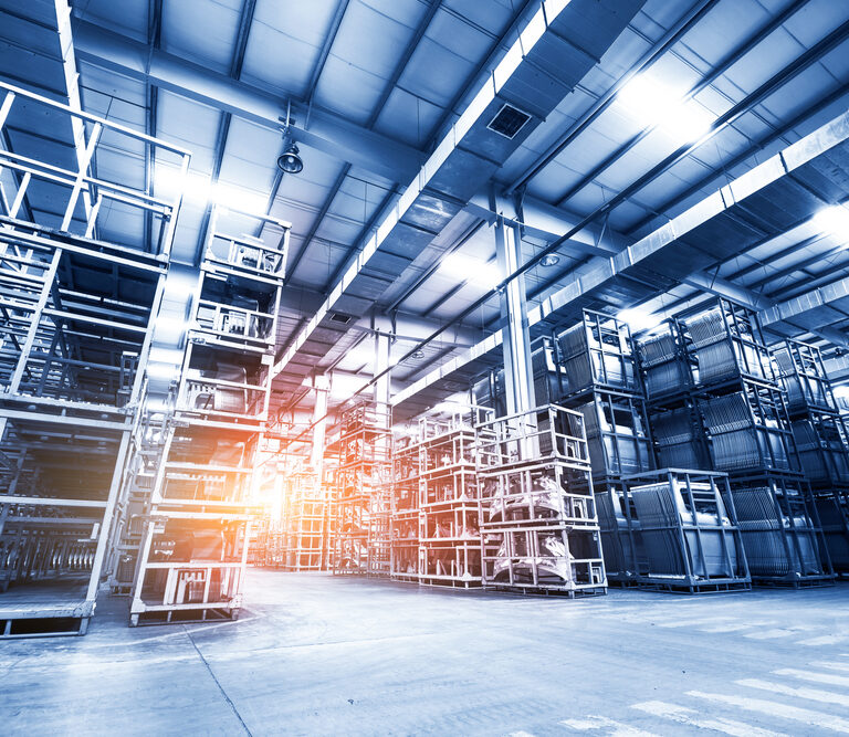 Large, modern warehouse interior with tall, empty metal shelving units and a high ceiling. Sunlight streams in from the left, highlighting the spacious industrial atmosphere—ideal for implementing slam line automation systems.