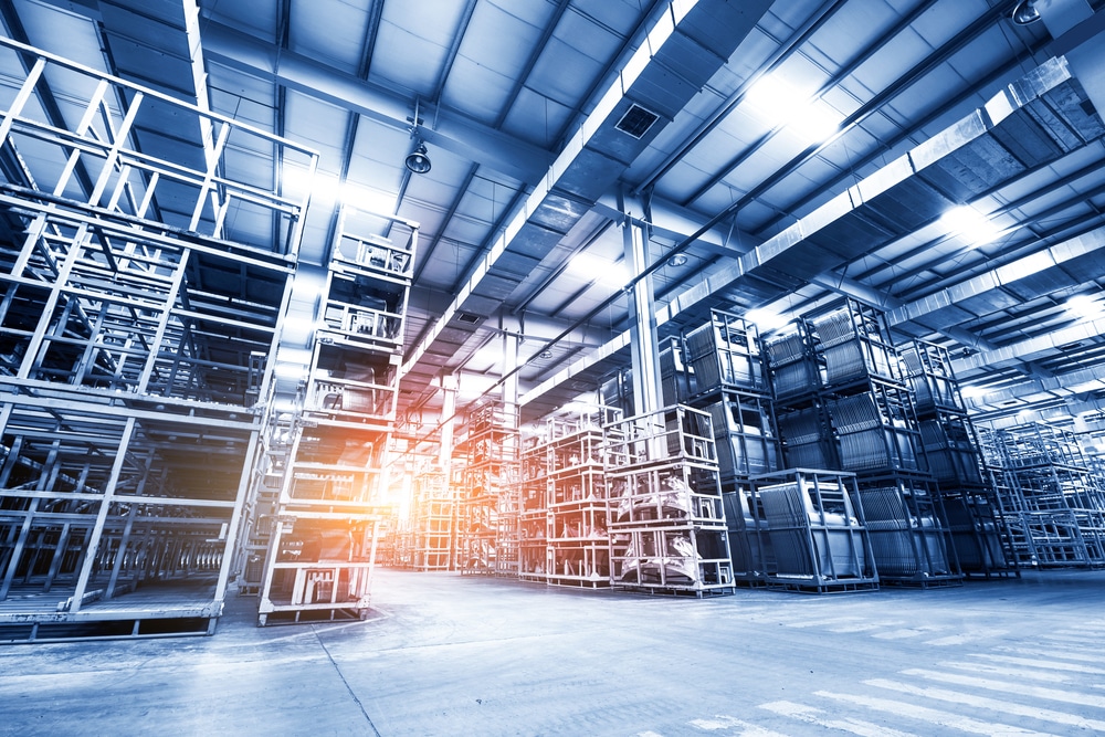 Large, modern warehouse interior with tall, empty metal shelving units and a high ceiling. Sunlight streams in from the left, highlighting the spacious industrial atmosphere—ideal for implementing slam line automation systems.