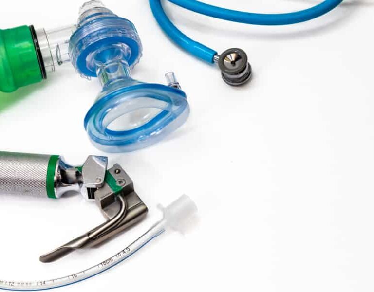 A close-up of medical equipment, including a green manual resuscitator, blue oxygen mask, laryngoscope, endotracheal tube, and stethoscope on a white background—ideal for illustrating a WMS Implementation Case Study in healthcare settings.