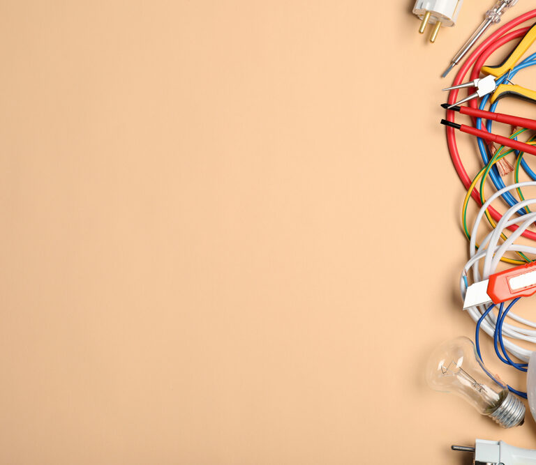Assorted electrical tools, wires, plugs, and light bulbs are arranged on the right side of a beige background, with empty space on the left.