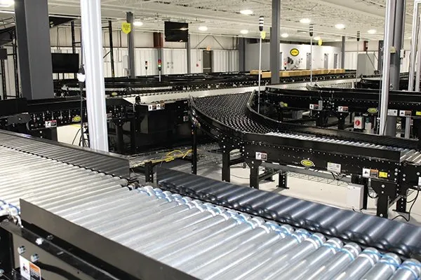 A large indoor facility with several interconnected conveyor belts, metal rollers, machinery, and Hytrol replacement parts, used for sorting or transporting packages in an industrial or warehouse setting.