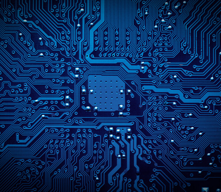 Close-up of a blue computer circuit board showing intricate electronic pathways and components, including a central microchip area with numerous connecting lines and soldering points.