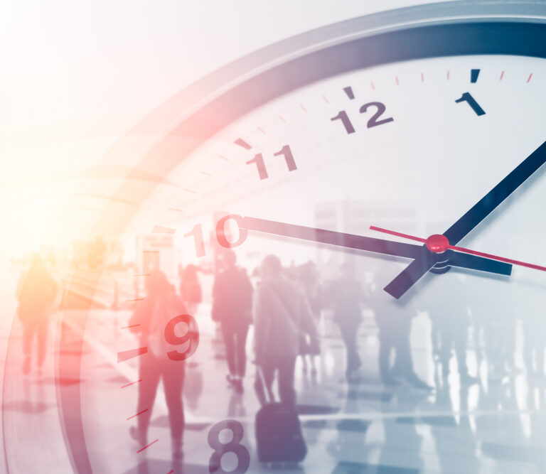 A close-up of a clock face showing the time as 10:09, with a blurred background of people walking in a brightly lit indoor space, creating a sense of motion and passing time.
