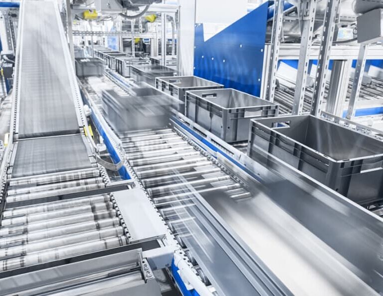 Automated conveyor system with gray plastic bins moving quickly along metal rollers in a bright, modern warehouse or distribution center showcases how facilities automate processes for fast-paced, efficient operations. Motion blur highlights speed and productivity.