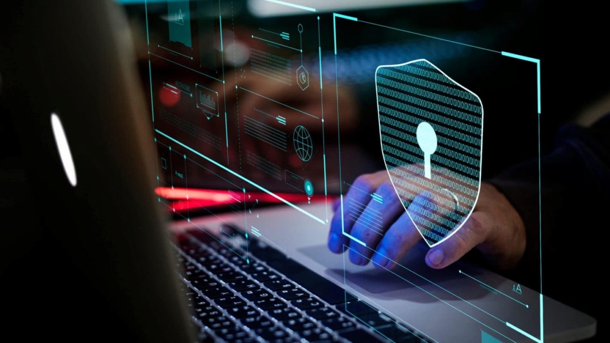 A person using a laptop with digital graphics overlaying the screen, including a large shield with a keyhole symbol, highlights cybersecurity and the cost of a security breach in protecting sensitive data.