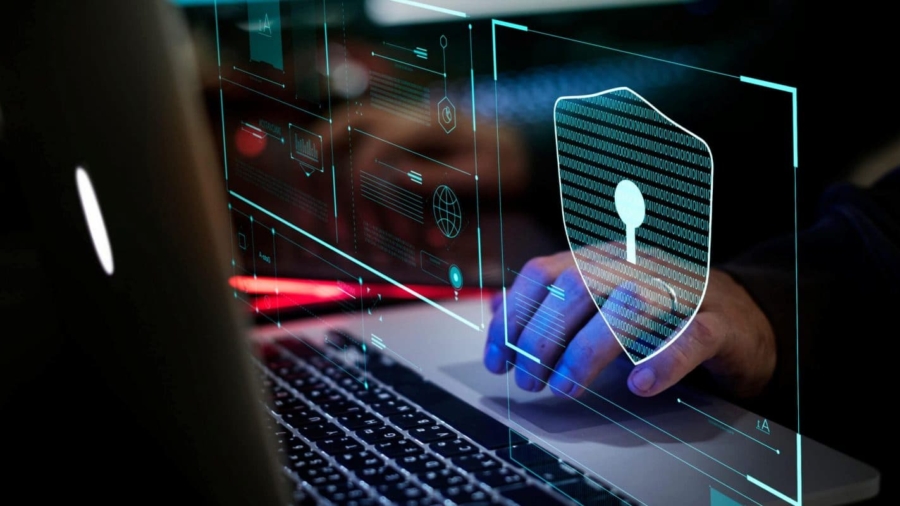 A person using a laptop with digital graphics overlaying the screen, including a large shield with a keyhole symbol, highlights cybersecurity and the cost of a security breach in protecting sensitive data.