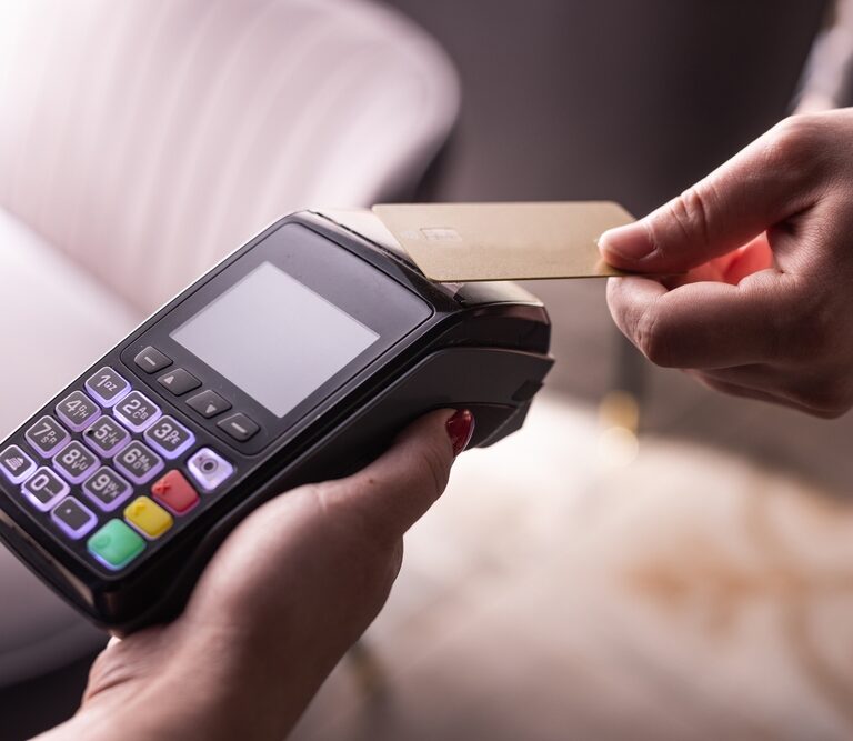 A person holds a payment terminal while another taps a gold credit card, showcasing how contactless payments can help automate everyday transactions.