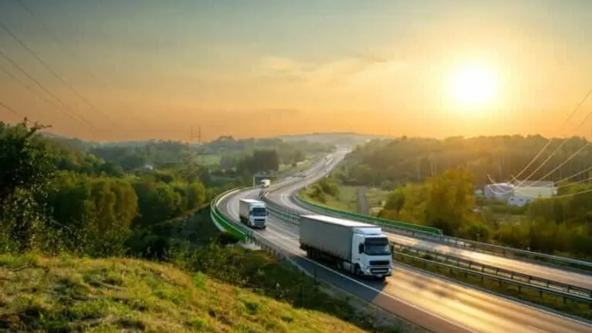 Several cargo trucks drive on a winding highway, showcasing an efficient transportation system surrounded by greenery during sunrise or sunset, with the sun shining brightly in a clear sky.