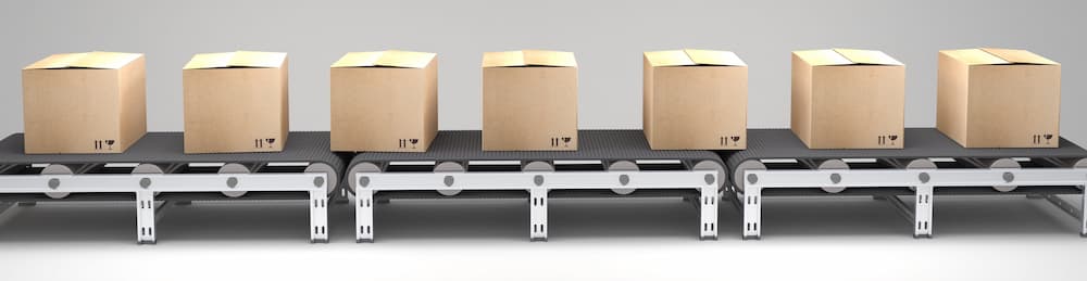 Seven closed cardboard boxes are evenly spaced on a moving goods-to-person conveyor belt against a plain light background.