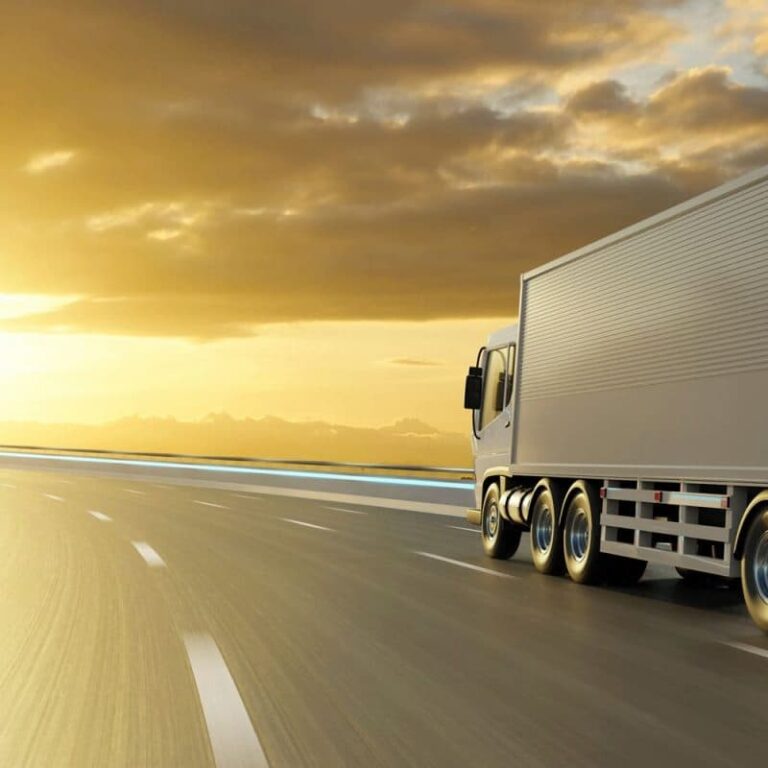 A large white semi-truck drives along a curving highway at sunrise or sunset, with tariffs shaping its journey as dramatic sky and sunlight illuminate the road ahead.