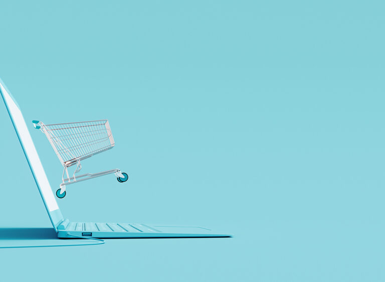 A shopping cart emerges from the screen of an open laptop on a light blue background, symbolizing online shopping and highlighting 2025 Retail Fulfillment Trends.