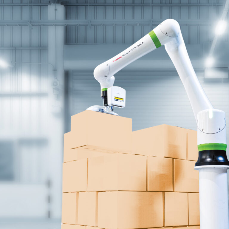 A robotic arm is stacking cardboard boxes in a warehouse with a bright, industrial interior. The background shows metal structures and large doors.