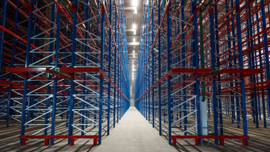 Empty metal storage racks extend in symmetrical rows inside a large warehouse, creating a sense of depth and perspective—an ideal setting for ai-powered inventory systems. Bright lights illuminate the clean concrete floor and steel framework.