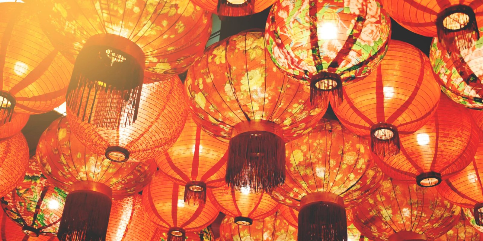A collection of red paper lanterns with floral patterns hanging closely together, illuminated with warm light, creating a festive and vibrant atmosphere.