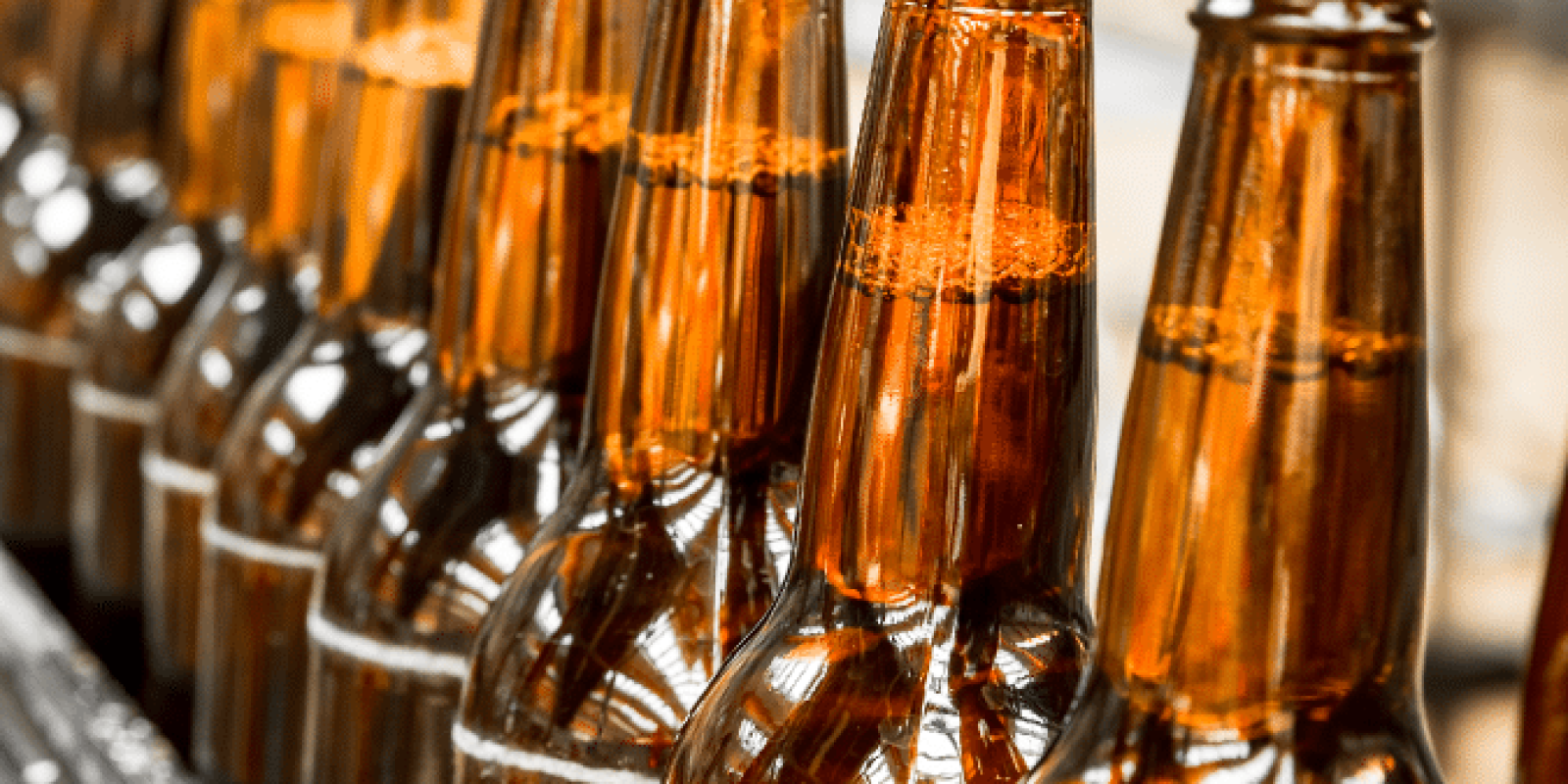 Close-up of amber glass beer bottles with caps, lined up in a row on a conveyor belt in a brewery or bottling facility.