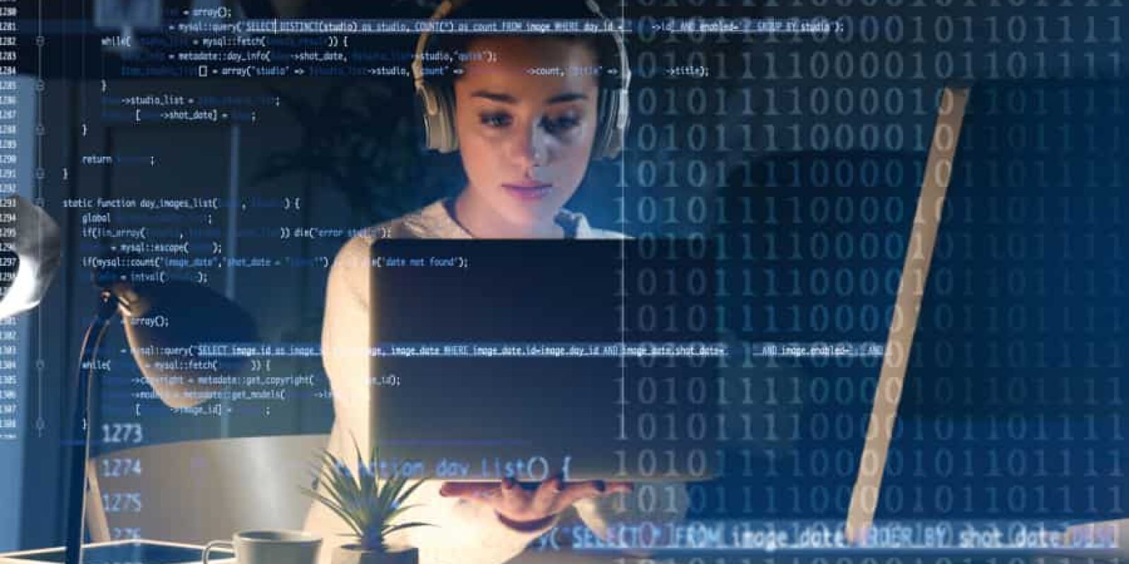 A woman wearing headphones works on a laptop at a desk, overlaid with blue computer code and binary numbers, suggesting programming or cybersecurity activity in a modern workspace.