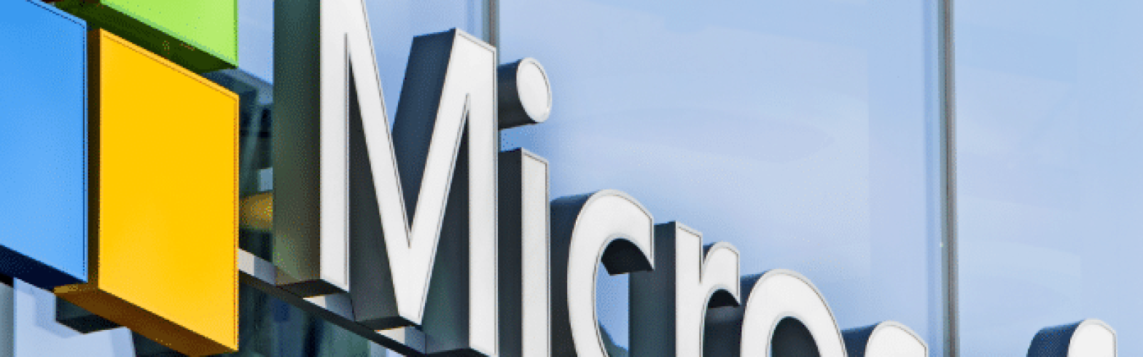 The Microsoft logo, featuring four colored squares and the word Microsoft in large white letters, is displayed on the exterior of a modern glass building.