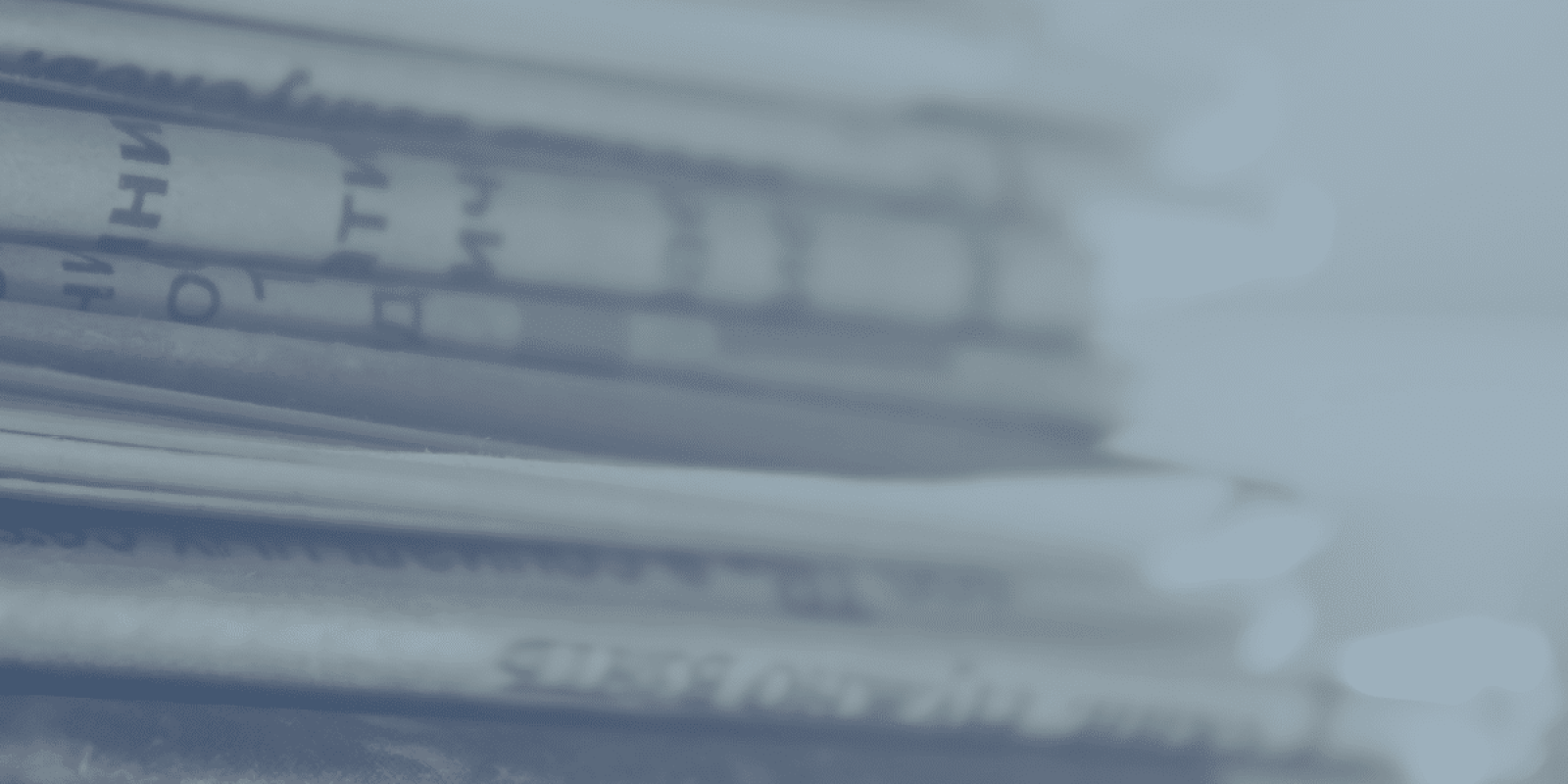 A close-up view of a stack of newspapers, with printed text visible on the pages. The image has a blue tint and a blurred background.