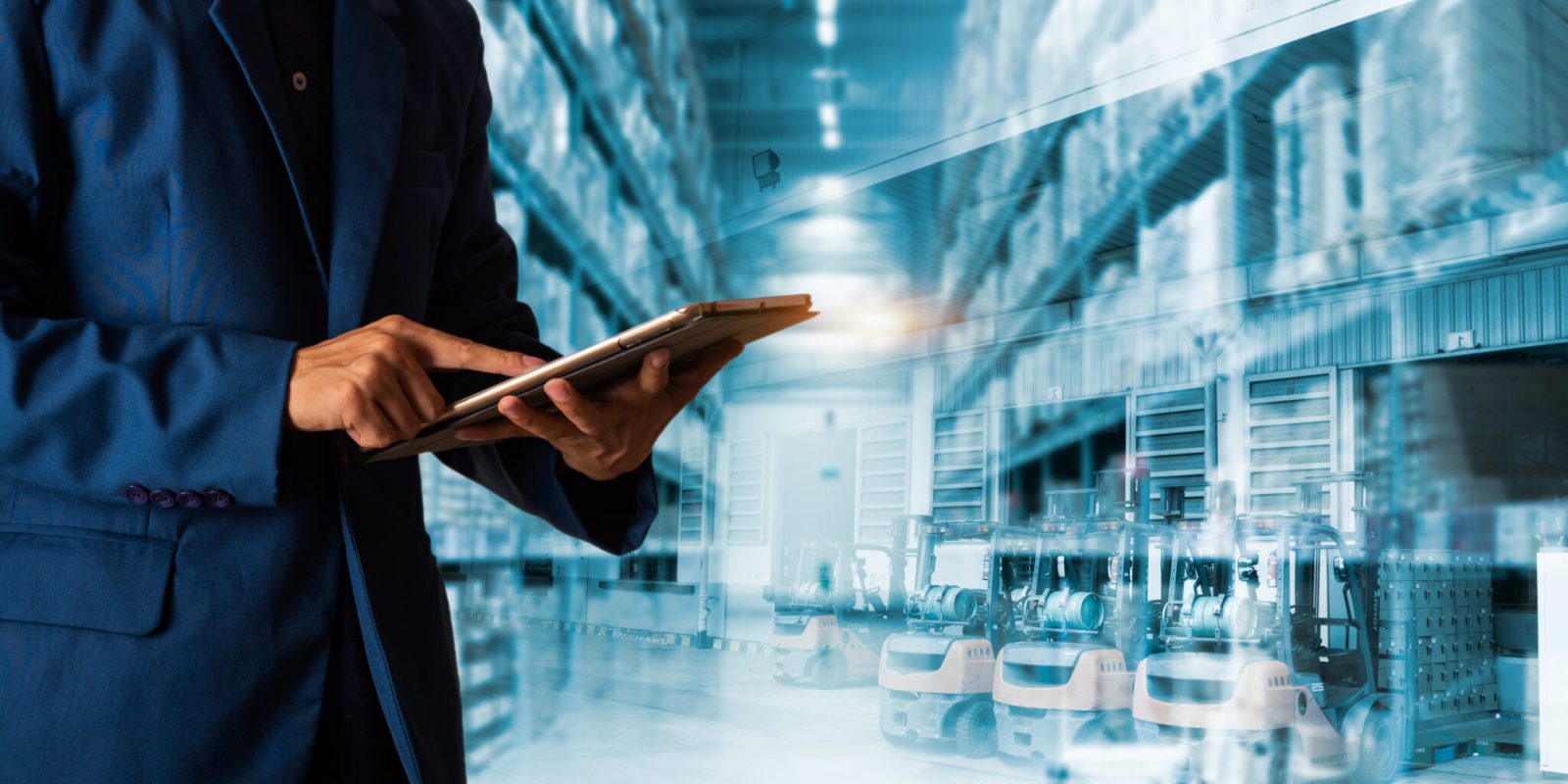 A person in a blue suit uses a tablet, standing in a warehouse with high shelves and rows of forklifts, representing modern inventory management and logistics technology.