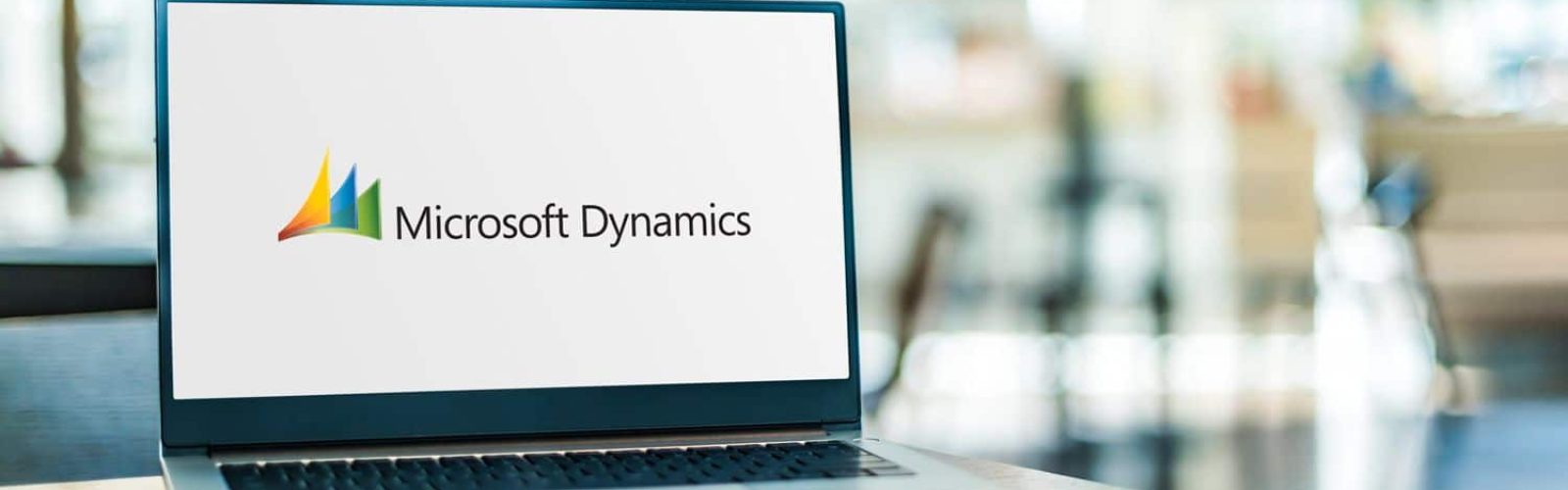A laptop on a table displays the Microsoft Dynamics logo on its screen, with a blurred indoor background.