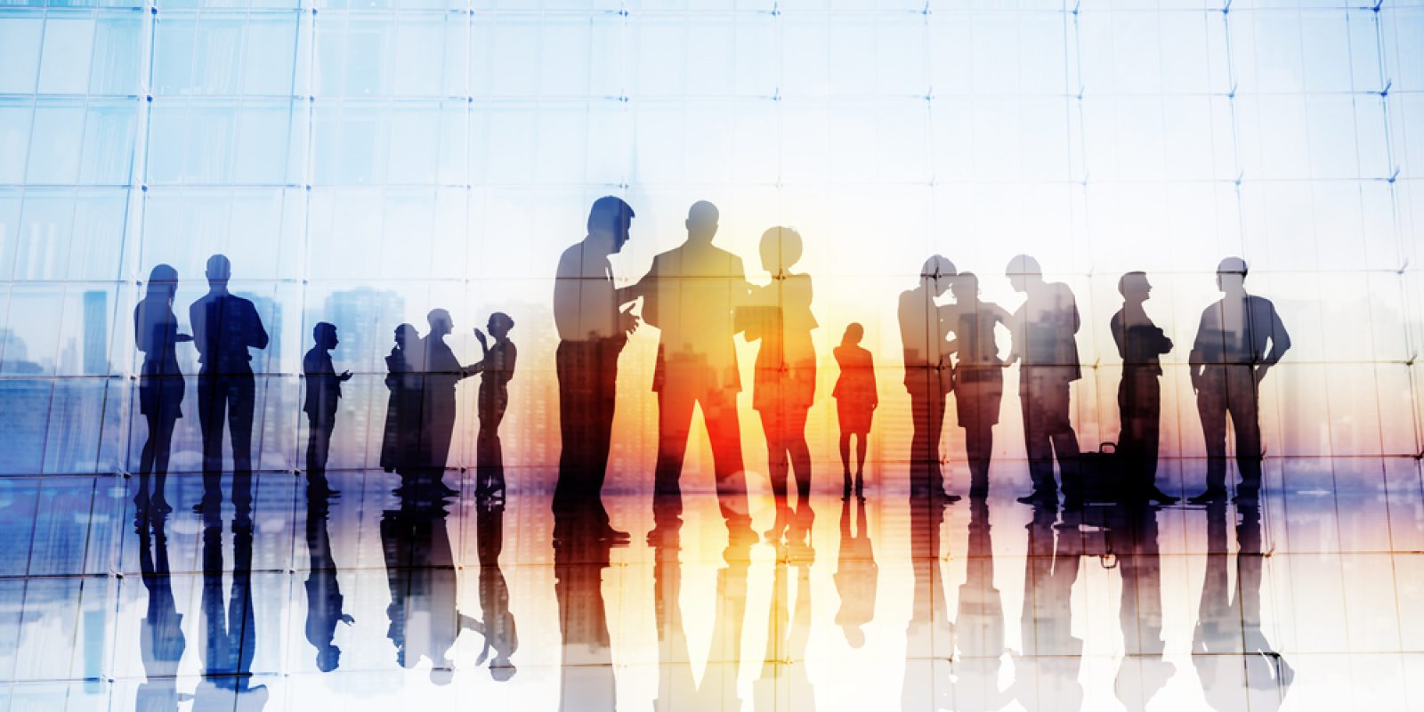 Silhouettes of business people standing and talking in groups against a large glass window, reflecting on the shiny floor as they discuss S&OP strategies in the soft sunset light.