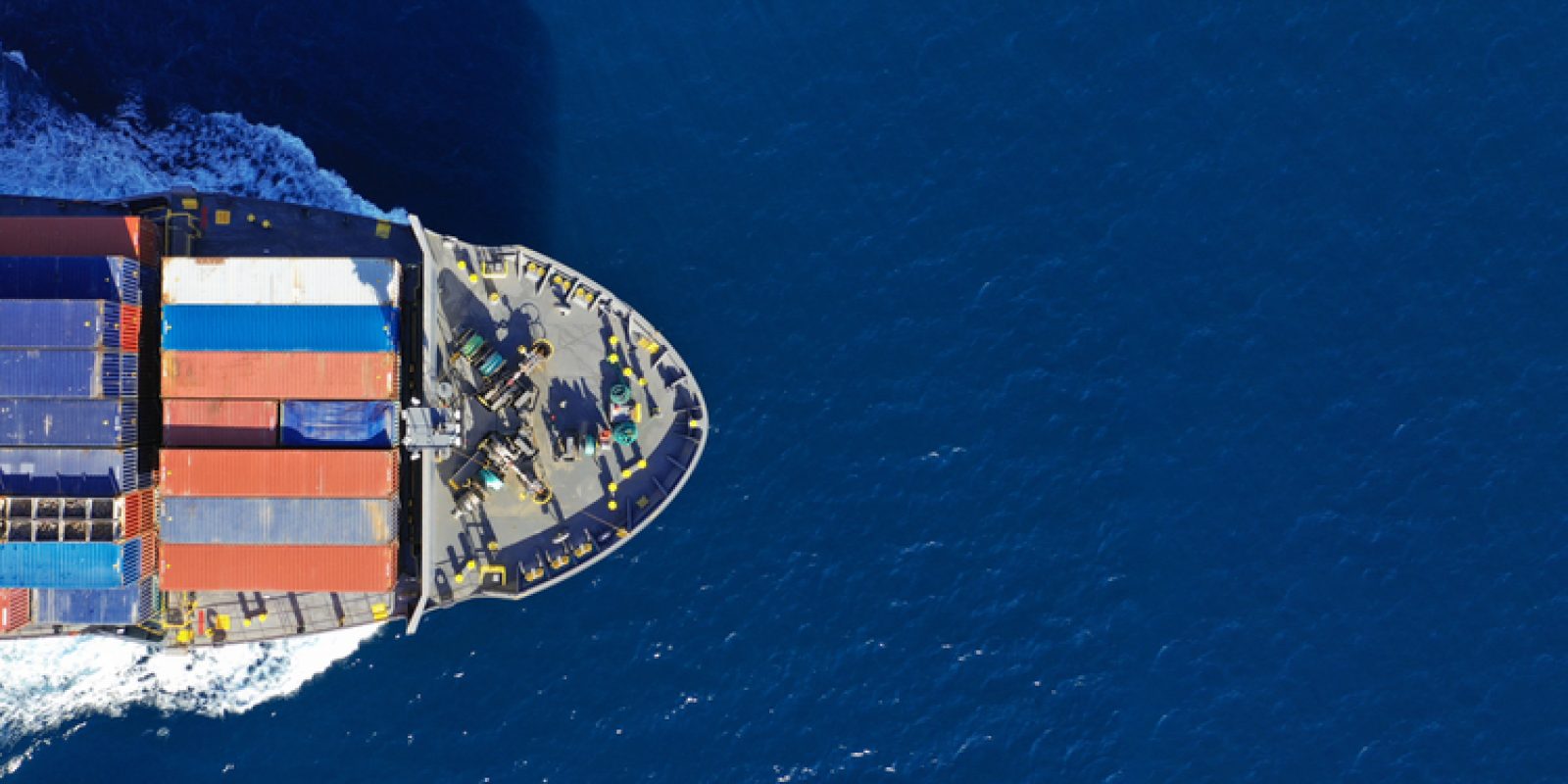 Aerial view of a cargo ship carrying colorful shipping containers, sailing through deep blue ocean water—powered by a skilled workforce ensuring smooth global trade.