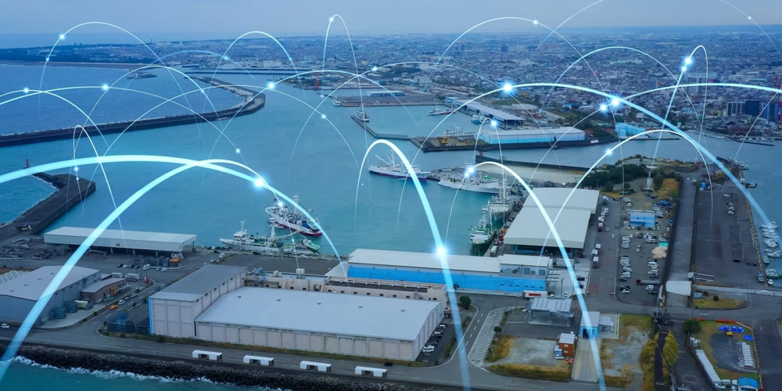 Aerial view of a busy port with warehouses, ships, and blue water. Digital lines and glowing points are overlaid, symbolizing a responsive supply chain with seamless network connectivity and efficient data transfer across the port.