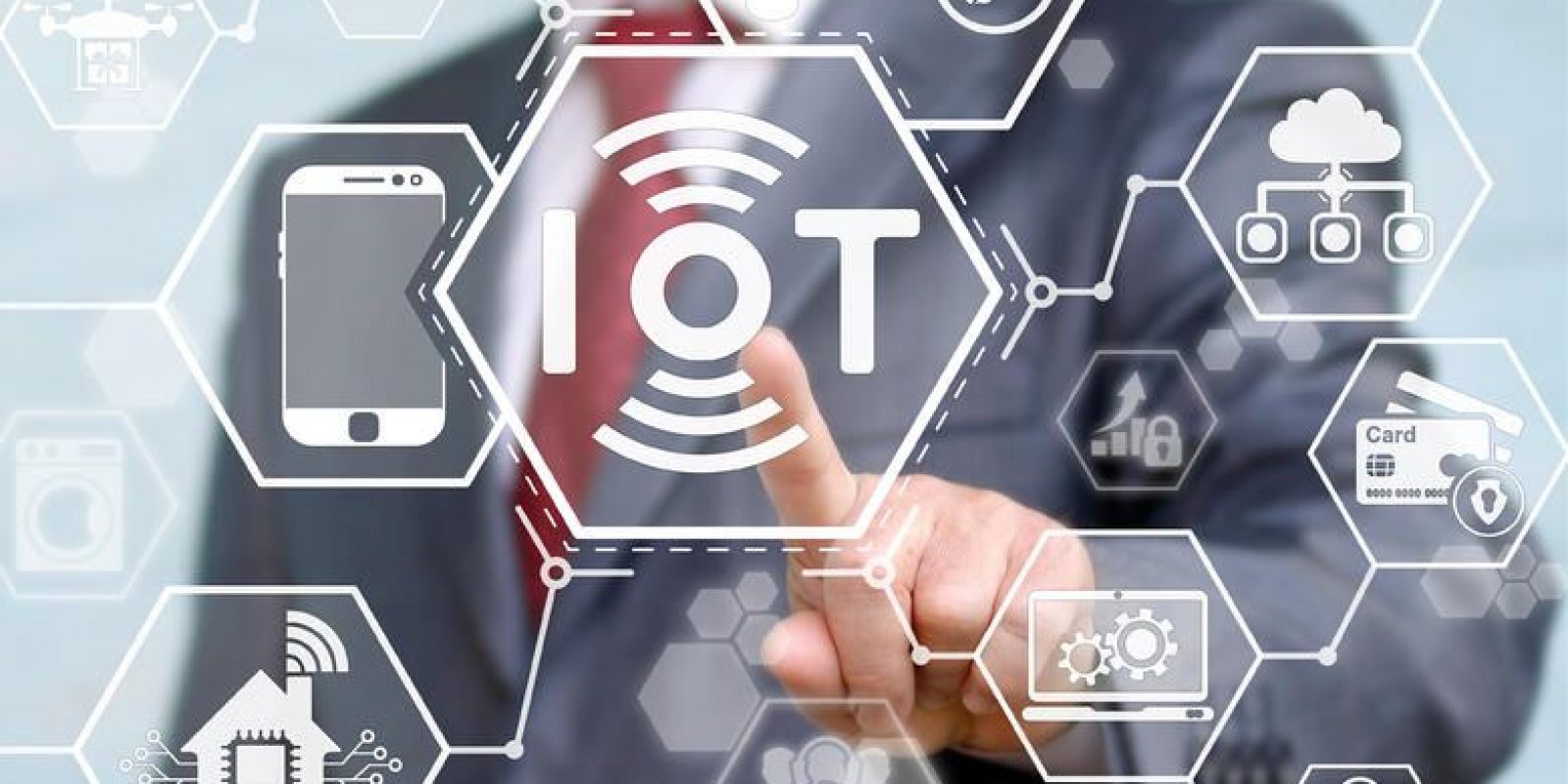 A person in a suit touches a virtual touchscreen with the word IOT at the center, surrounded by hexagonal icons representing technology and Internet of Things devices, such as a phone, house, and car.