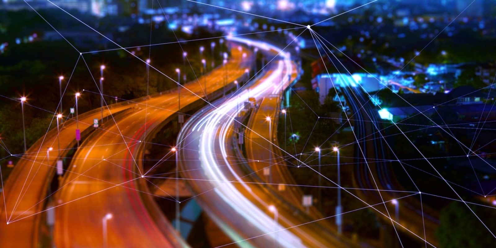Blurred night view of a city highway with light trails from cars, overlaid with digital network lines suggesting connectivity, smart technology, and modern urban infrastructure.