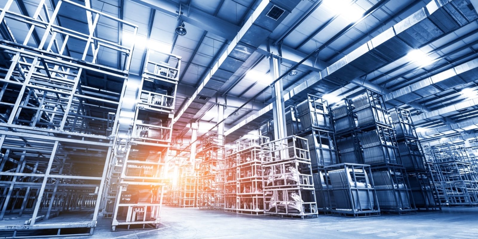 Large, modern warehouse interior with tall, empty metal shelving units and a high ceiling. Sunlight streams in from the left, highlighting the spacious industrial atmosphere—ideal for implementing slam line automation systems.