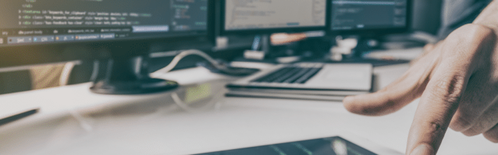 A person interacts with a tablet displaying code, while multiple computer monitors in the background also show programming code in a modern workspace.